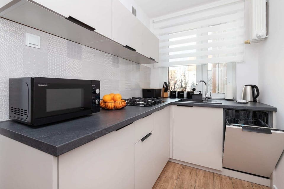A modern kitchen with dark countertops, white cabinets, and fully equipped with appliances like a microwave and kettle.
