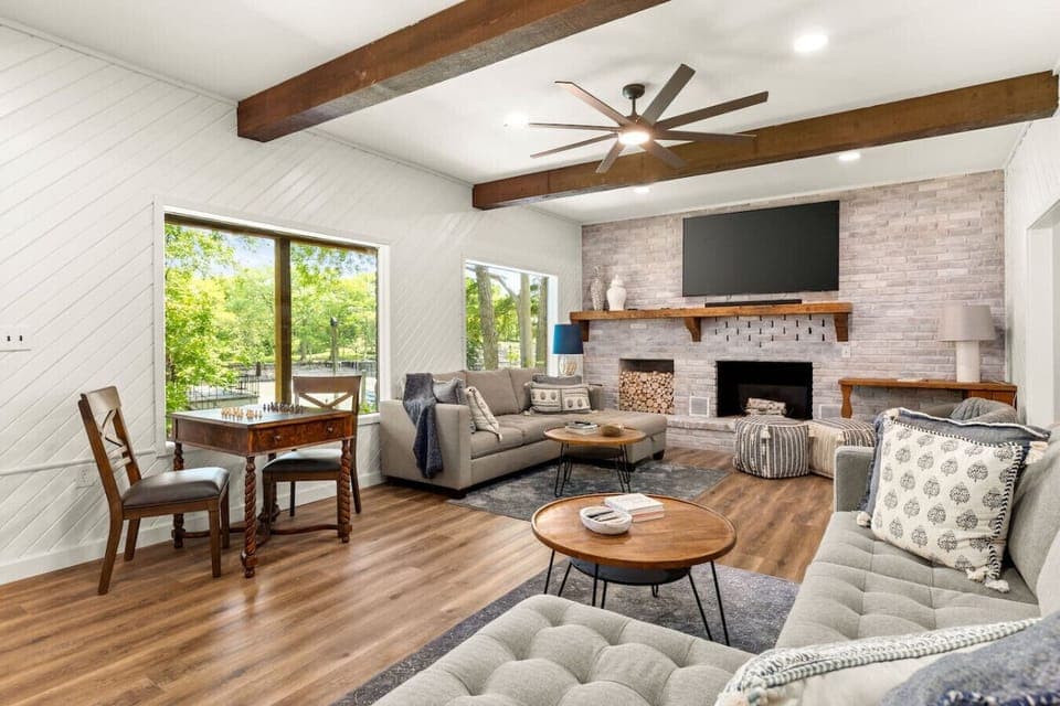 Spacious open-concept living room with vaulted ceilings, exposed wood beams, a cozy fireplace, and plenty of seating—perfect for gathering, relaxing, and movie nights together.