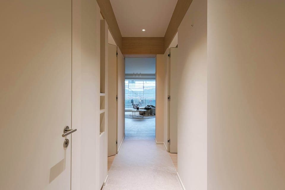 Bright, modern hallway leading to a stylish living area with large windows and natural light—creating a welcoming and airy atmosphere from the moment you enter.
