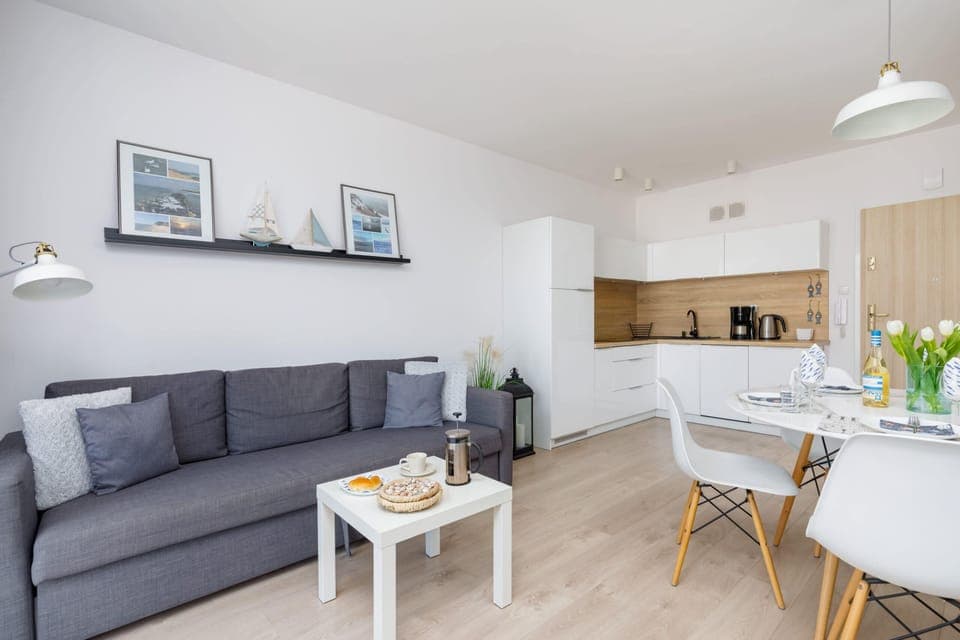 A cozy living area featuring a grey sofa, white coffee table, and natural light from a large window.
