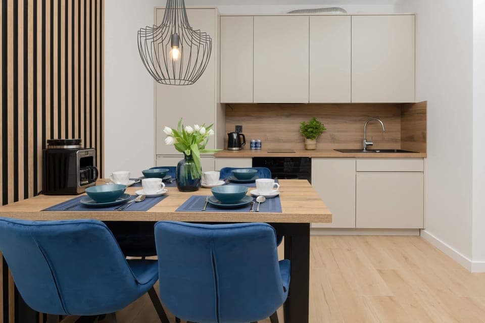 A dining area with blue chairs and a wooden table, adjacent to a modern kitchen with sleek cabinetry.
