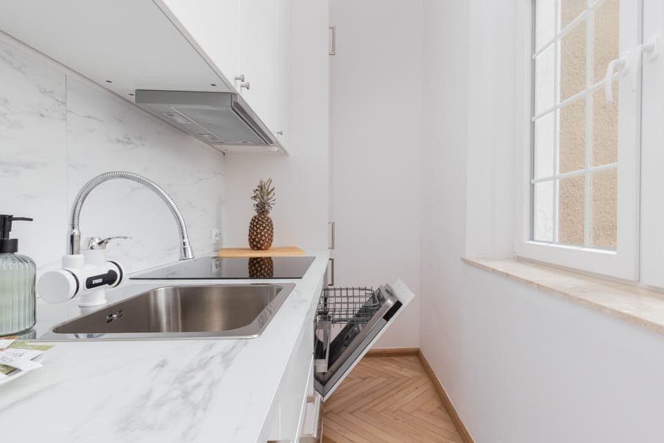 A bright and modern kitchen area with a marble countertop, sink, and white appliances for a clean look.
