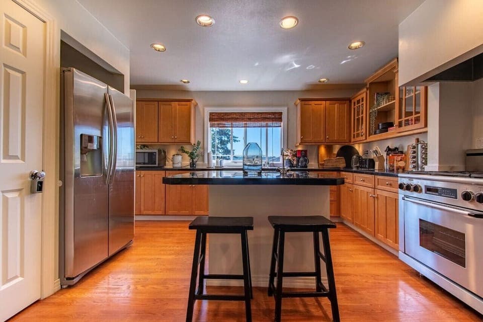 The kitchen features a very large island, gas range stovetop, two sinks, and a large stainless steal refrigerator.