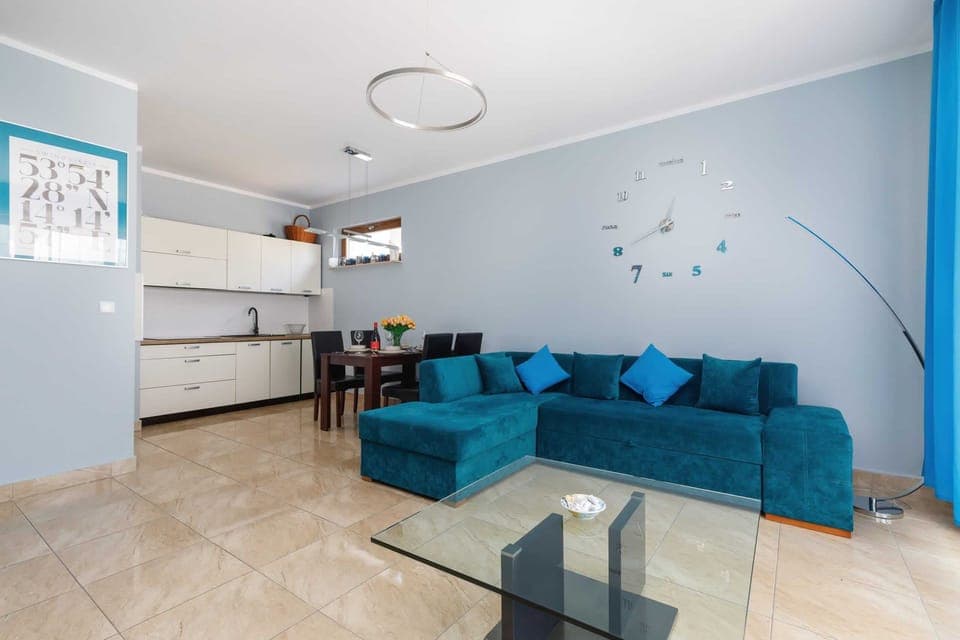 A bright, modern living room with a turquoise sofa, decorative pillows, and a flat-screen TV mounted on the wall.