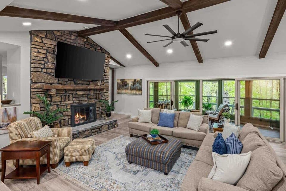 Unwind by the stone fireplace in this light‑filled living room with vaulted ceilings, exposed beams and a 75″ smart TV.