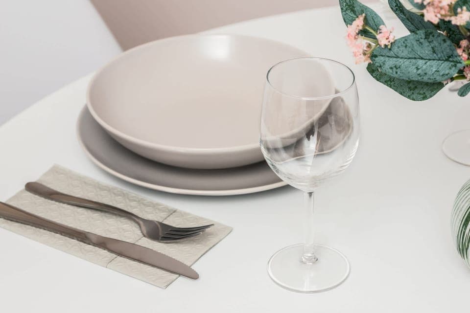 A set table with elegant dishes, wine glasses, and a flower centerpiece, ready for a meal.