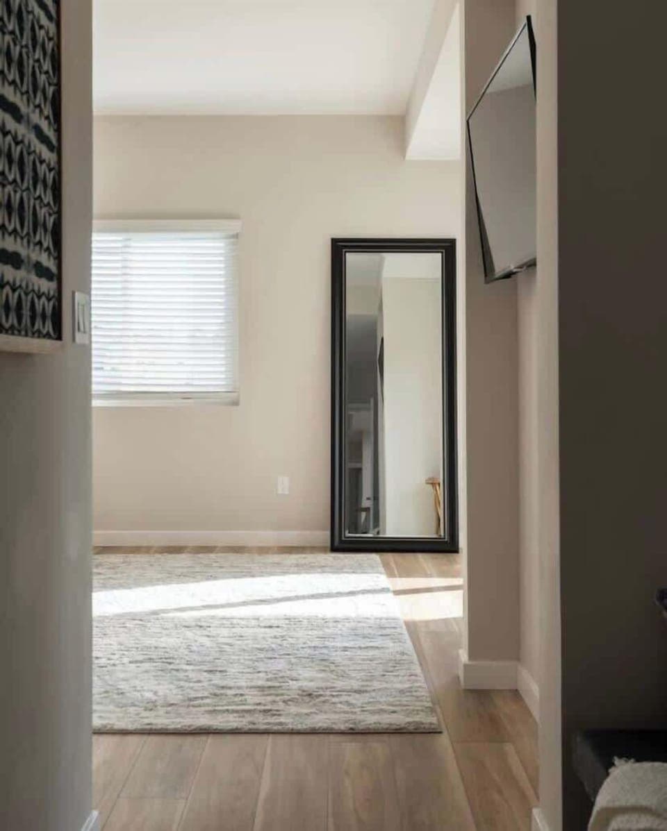 The sleek black-framed mirror adds depth and elegance to the space, making it feel more open and bright. The neutral tones and minimalist design create a calming, modern atmosphere. 
