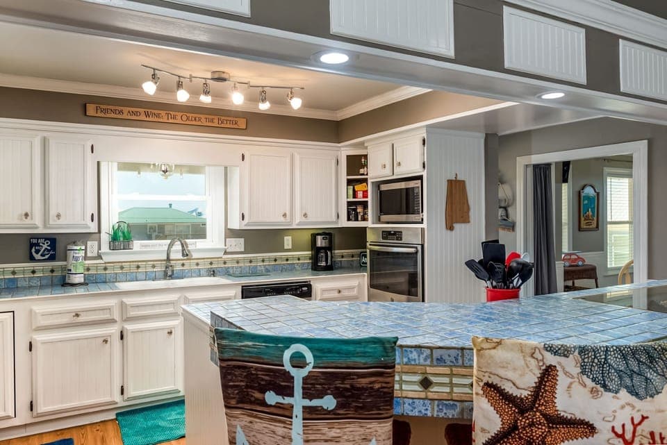 Your fully equipped kitchen features coastal charm with white cabinets, tile counters, and modern appliances—perfect for preparing meals with ocean views.