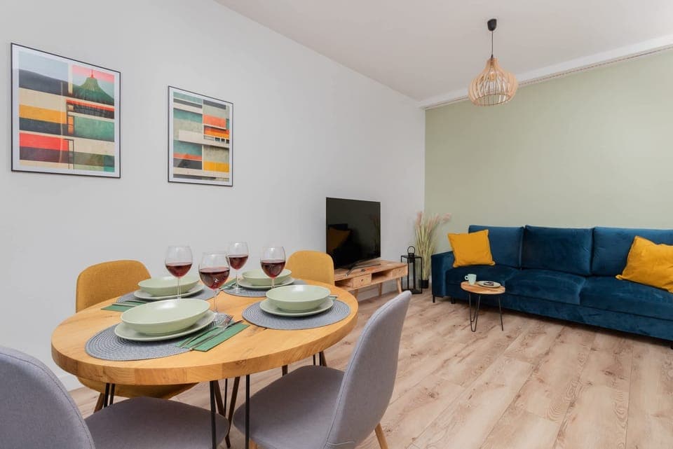A bright and modern dining and living area with a round table, colorful chairs, and a blue sofa with yellow cushions.
