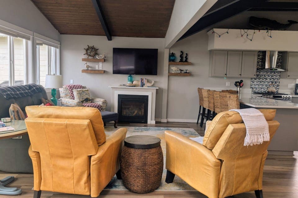The wood-lined & beamed vaulted ceiling in the living room is supported by floor-to-ceiling windows and views of the beach grass and ocean sky.