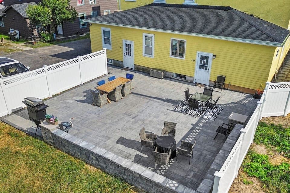 A sun-kissed yellow house, nestled in an open and spacious setting, features a welcoming porch adorned with comfortable seating.