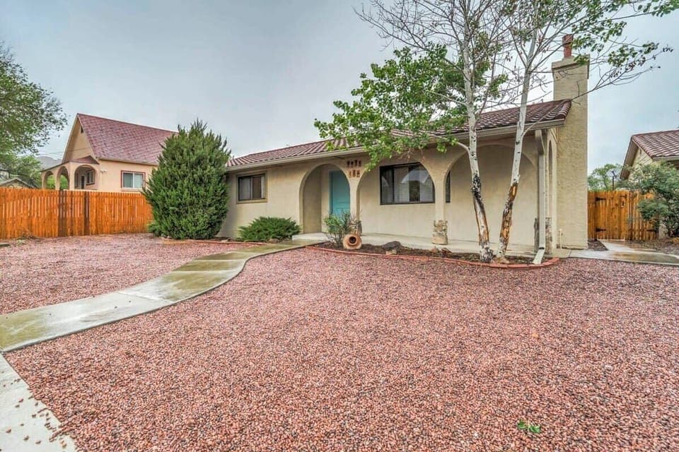 Unit A Main House - Classic stucco home with an arched entry and wide gravel yard—easy arrival, easy lounging. Follow the curved path to the front door beneath tall shade trees.