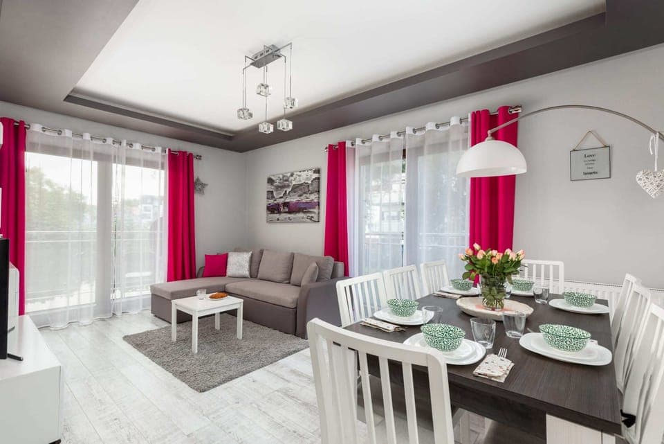 A sleek dining space with a white table and chairs, accompanied by bold pink curtains and modern decor.
