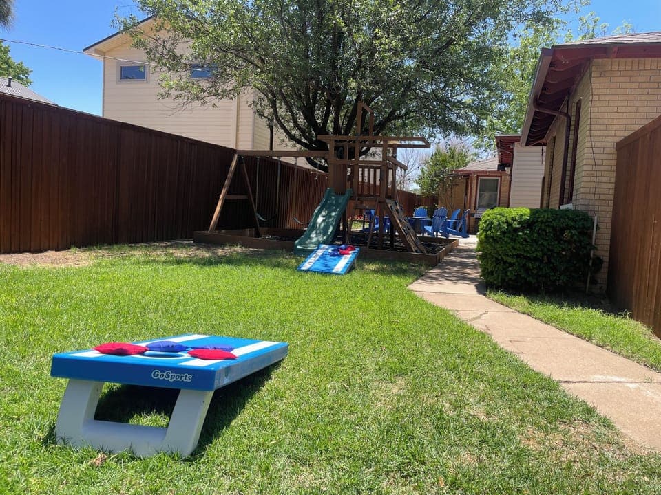 Fully enclosed back yard with a fire pit, grill, chairs, play set and corn hole.