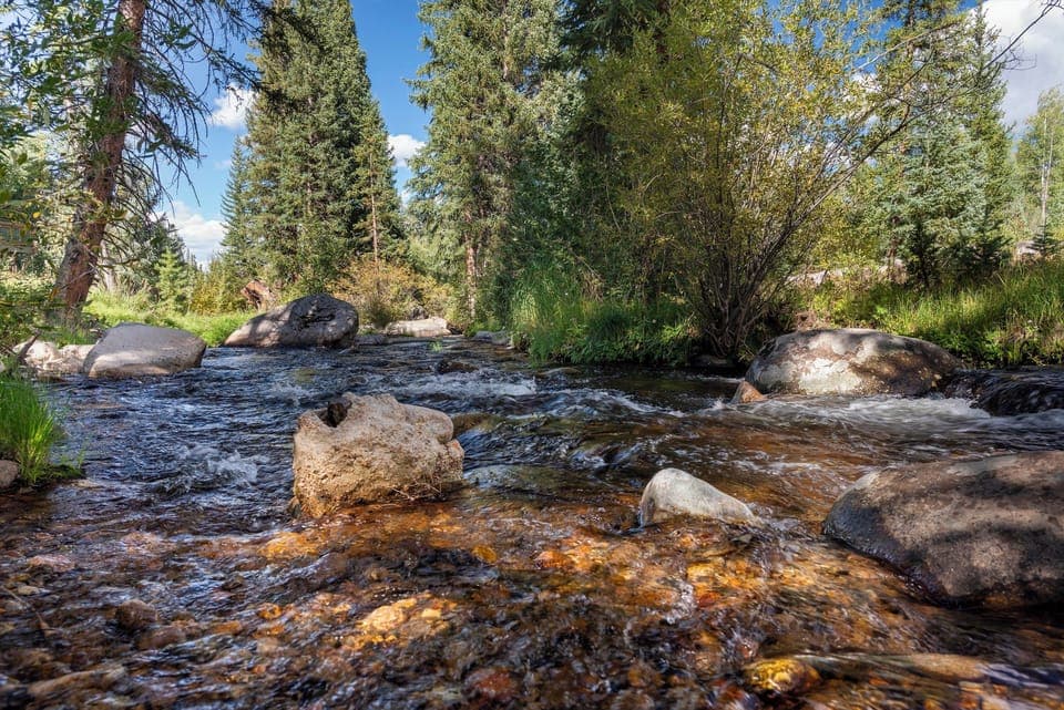 A pristine mountain stream flows through the scenic landscape near the property, surrounded by towering evergreens and natural boulder formations.