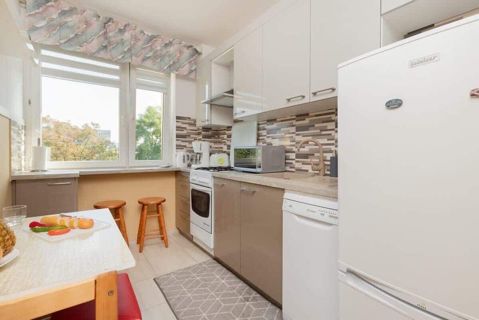 A compact kitchen with white cabinetry, tiled backsplash, and a window offering natural light.

