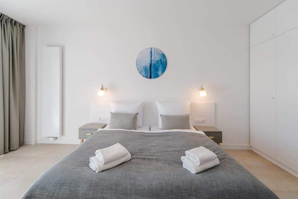 A bright bedroom with a double bed, gray bedding, and two bedside lamps, complemented by modern wall decor.

