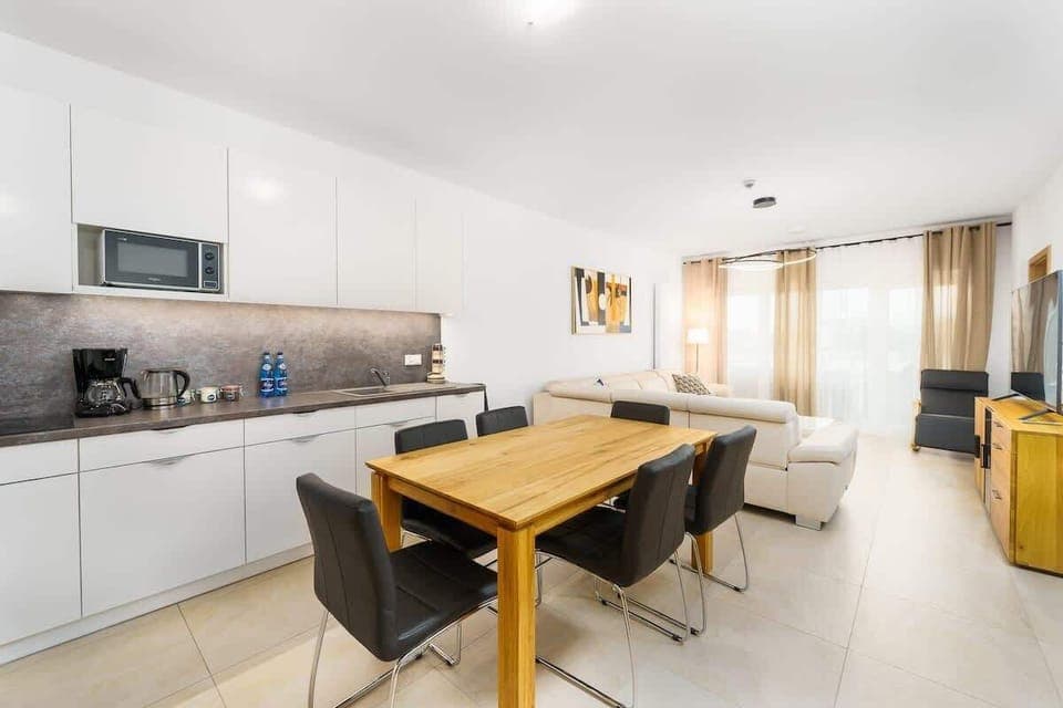 A modern kitchen with white cabinetry, a wooden dining table, and a gray backsplash, blending functionality with style.
