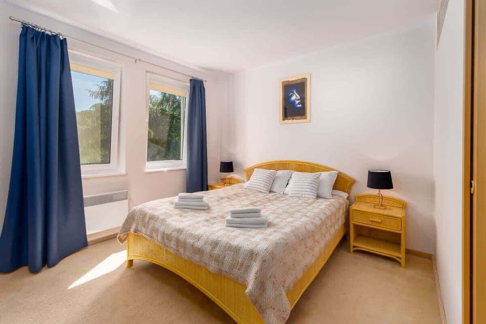 A bedroom with a double bed, wooden furniture, and large windows with blue curtains, offering a welcoming vibe.
