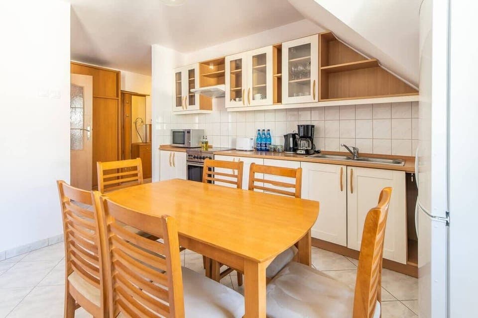 A dining area with a wooden table and chairs, adjacent to an open kitchen with a sloped ceiling.

