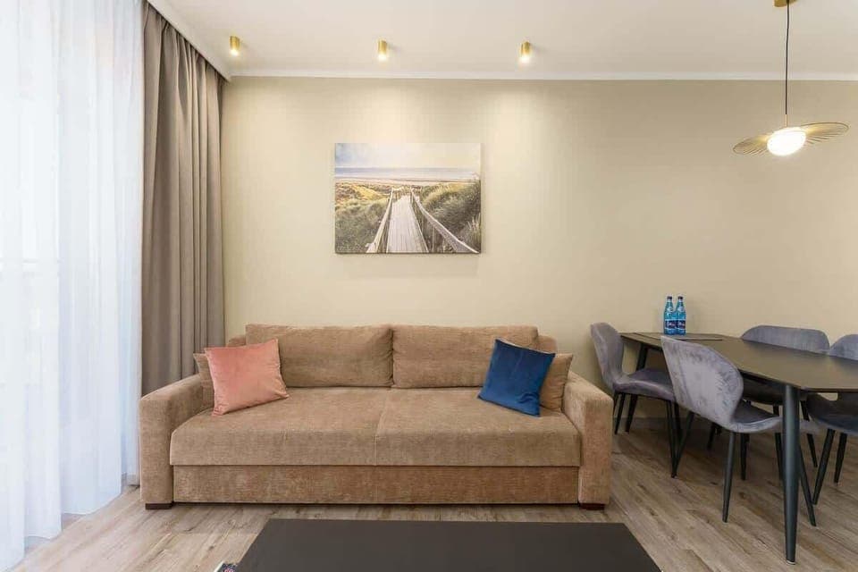 A cozy living and dining area with a sofa, a dining table, and large windows, creating a bright and inviting space.
