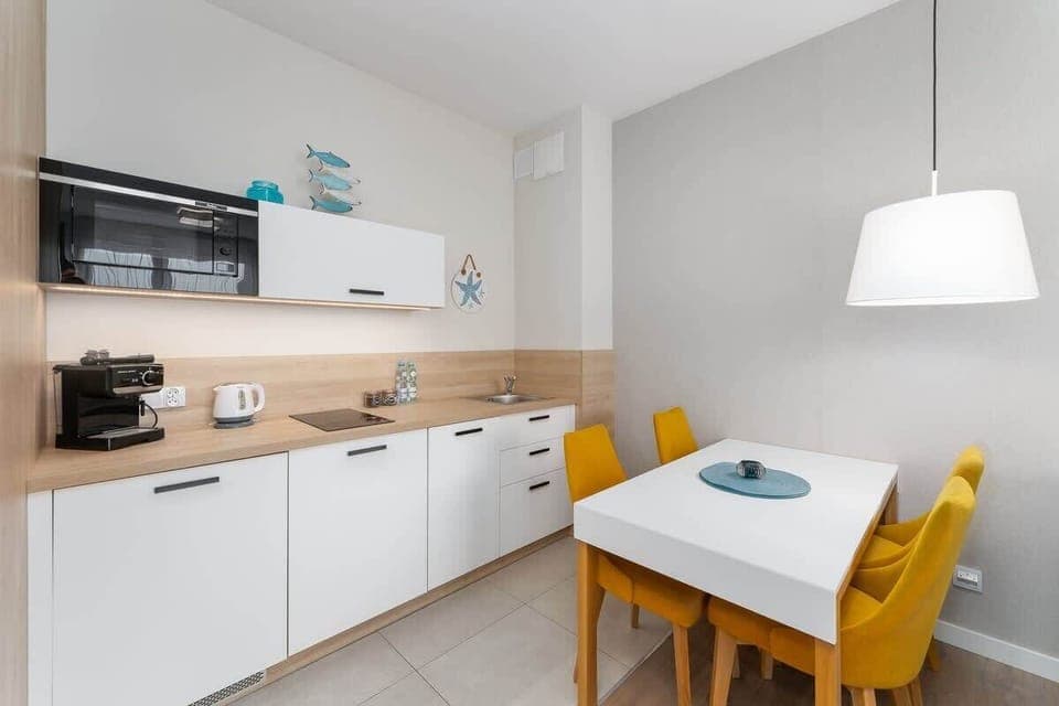 A sleek kitchen with white cabinetry, wooden accents, and a dining area with yellow chairs for a cheerful ambiance.
